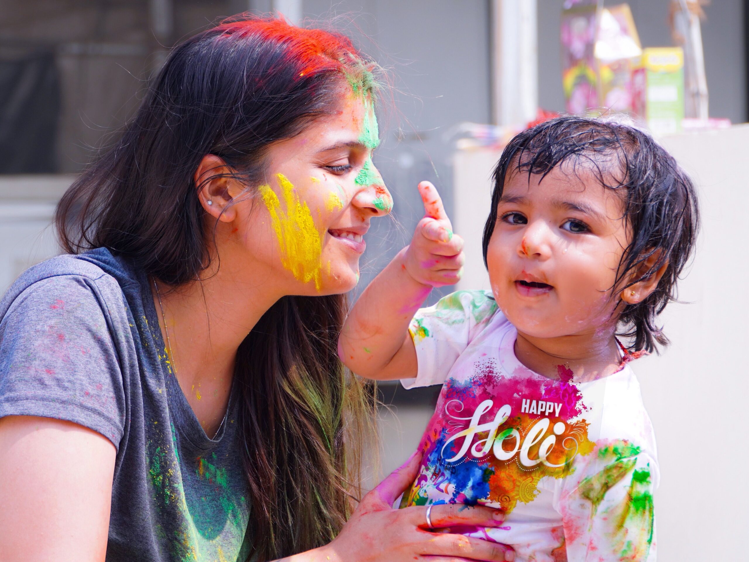 Woman and child enjoying vibrant Holi festival filled with colorful powders.