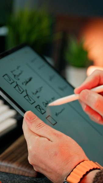 Close-up of hands using a stylus to write on a digital checklist, enhancing productivity.